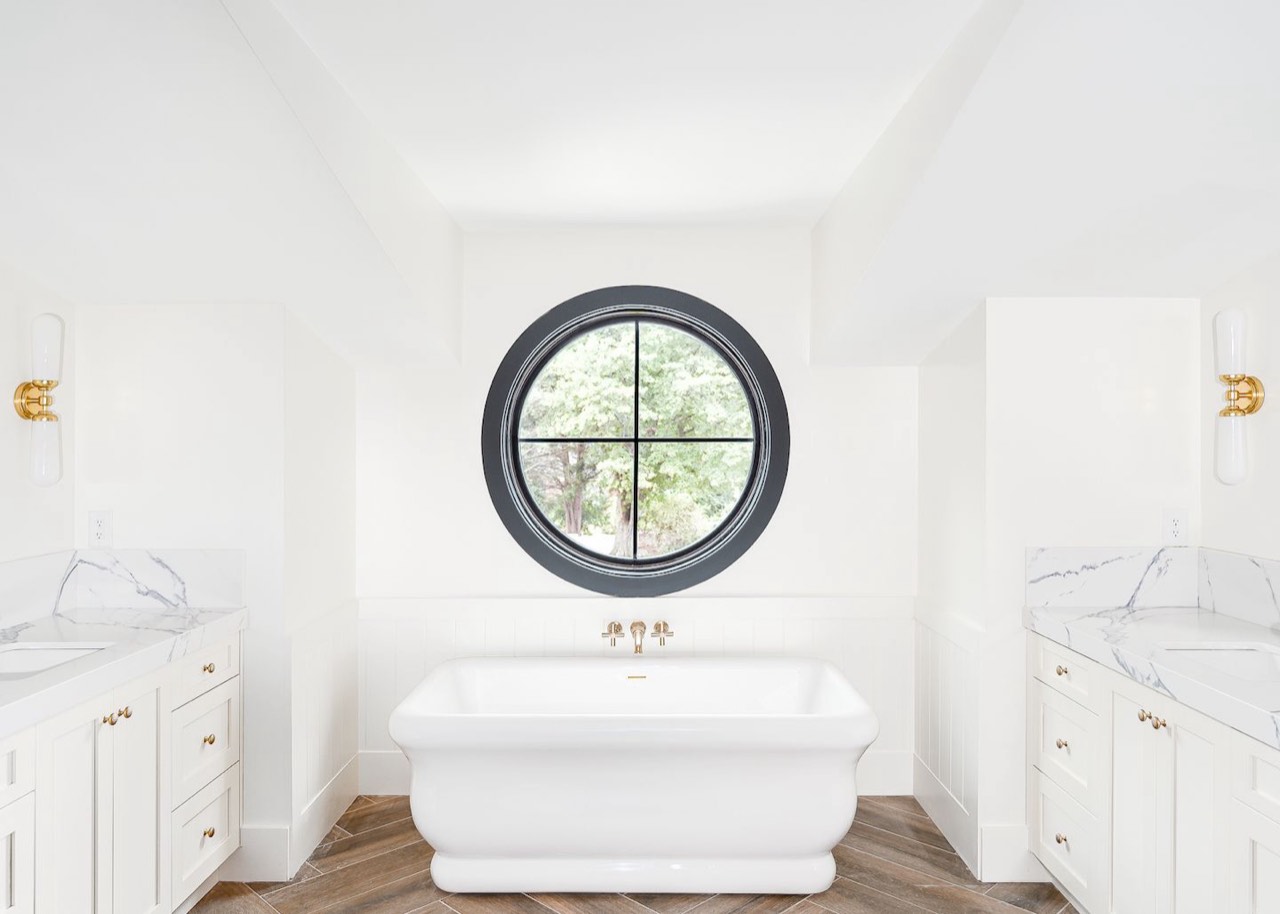 A round porthole window over a freestanding bathtub, with no window covering